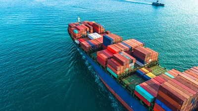 Image of a red and blue cargo ship heading out to sea with brightly freight containers on board
